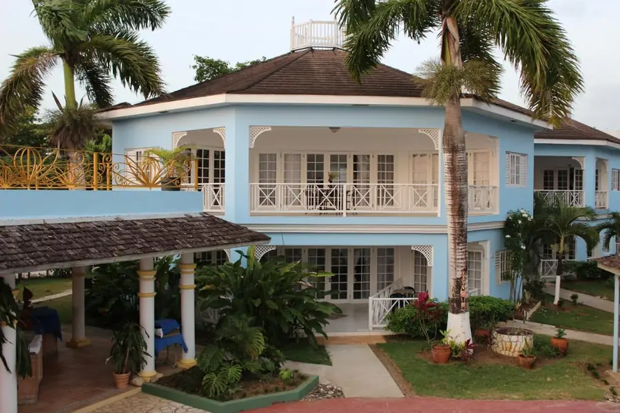 The main building of Beachcomber Club Resort, light blue with white balconies, among palm trees and garden